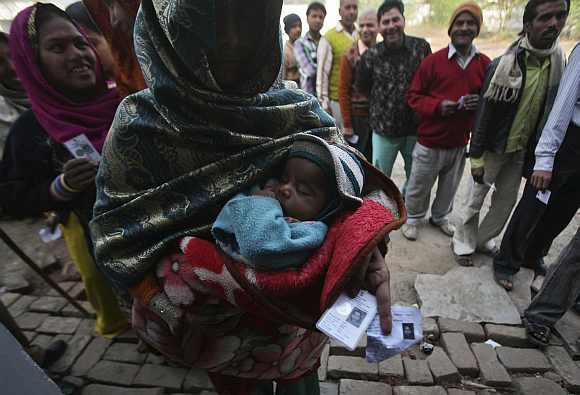 A woman holds her baby and her voter identity card as she waits for her turn to cast her ballot at a polling station