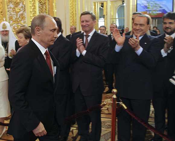 Putin walks in to attend the inauguration ceremony, with former Italian Prime Minister Silvio Berlusconi seen in the background, at the Kremlin in Moscow