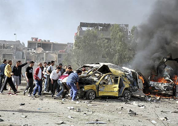 People and security personnel try to remove a car from an explosion site in Damascus