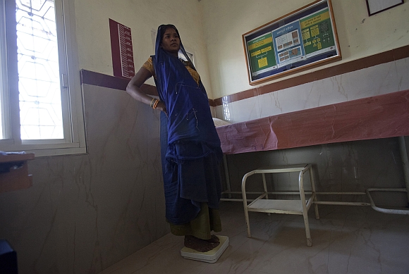 A 26-year-old pregnant woman in labour, stands on a weighing scale as her details are recorded at a community health centre in Chharchh, Madhya Pradesh