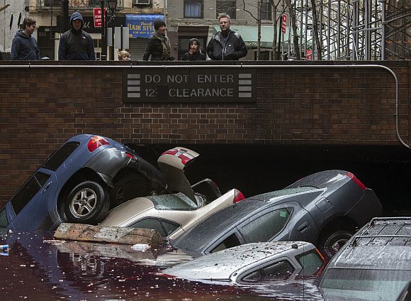 Residents stand over vehicles which were submerged in a parking structure in the financial district of Lower Manhattan