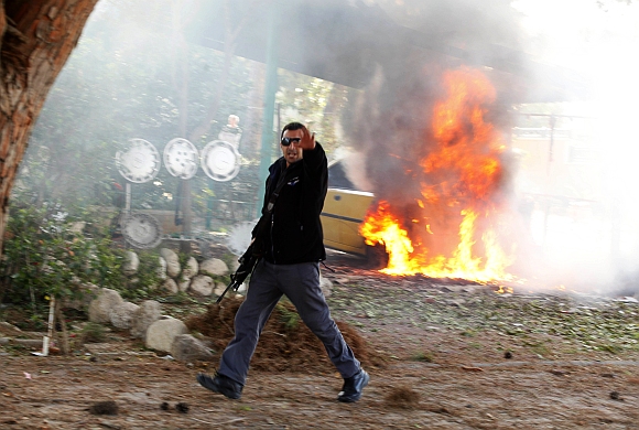 An Israeli police officer gestures in front of a burning car after a rocket fired by Palestinian militants in Gaza landed in the southern city of Ashkelon