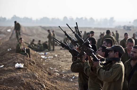 Israeli soldiers check their weapons at a staging area near the border with the Gaza Strip
