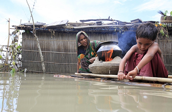 A woman cooks next to her child on a makeshift banana plant raft at a flooded village in Kurigram, Bangladesh