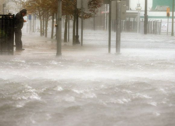 A man stands on a dry patch of sidewalk on a flooded street as Hurricane Sandy moves up the coast in Atlantic City, New Jersey
