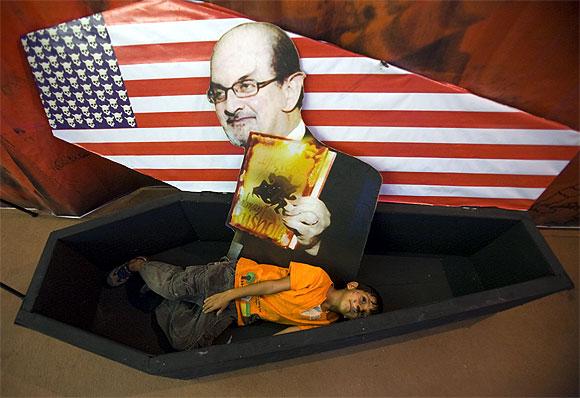 An Iranian boy lies in a symbolic coffin for the US with a picture of author Salman Rushdie