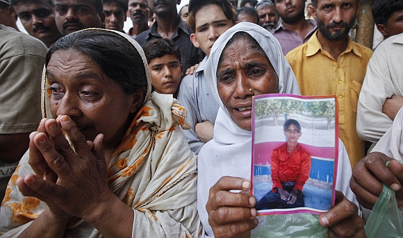 A woman holds a portrait of her son while waiting with others to identify his body