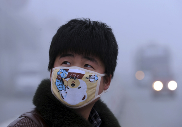 A man wearing a mask looks up as he walks on a street on a foggy day of Bozhou, Anhui province, China