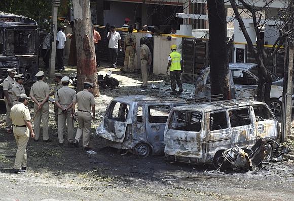 Policemen walk past damaged vehicles at the scene of a blast near the Bharatiya Janata Party office in Bangalore