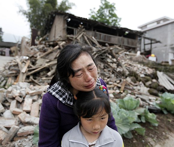 Song Zhengqiong, holding her daughter, cries in front of her damaged house