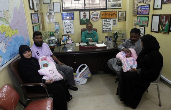 Childless couples sit with newly adopted babies, Fatima (L) and Zainab (R), whom Pakistani television talk show host Aamir Liaquat Hussain gave away on his show, as they pose for photographs at the Chhipa Welfare Association office in Karachi