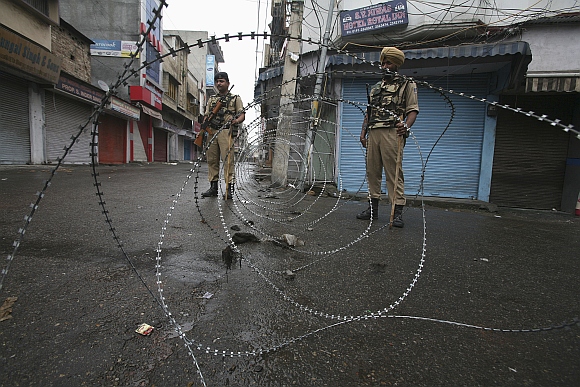 Policemen stand guard at a street during a curfew following riots, in Jammu