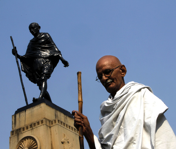 Mahesh Chaturvedi, dressed up like Mahatma Gandhi, poses for a photo in front of a statue of Gandhi in the old quarters of New Delhi