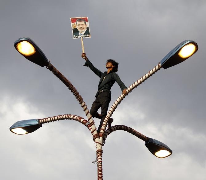 A supporter of deposed Egyptian President Mohamed Morsi holds up his photo while standing at the top of lamp posts during a march to show solidarity with his supporters in Egypt, in Sanaa