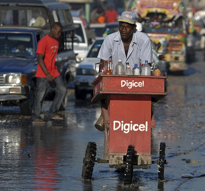 A man pushes his cart of mixed beverages through dirty water along a street in Port-au-Prince