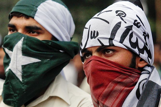 Supporters of the banned Islamic organisation Jamaat-ud-Dawa cover their faces with the Pakistan's national (left) and party flags during a protest