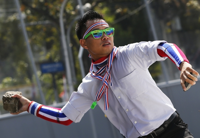 An anti-government protester wearing national colours throws a rock during clashes with police near the Government House in Bangkok