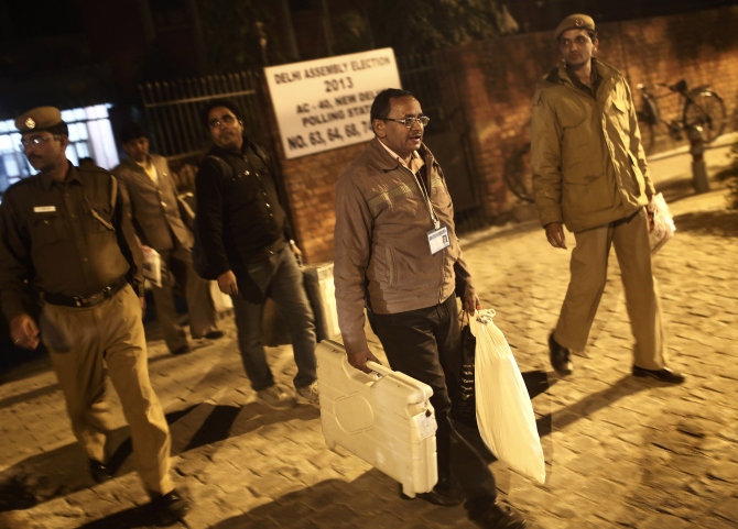 A polling officer carries electronic voting machines as he leaves a polling station at the end of polls, during the state assembly election in New Delhi. 