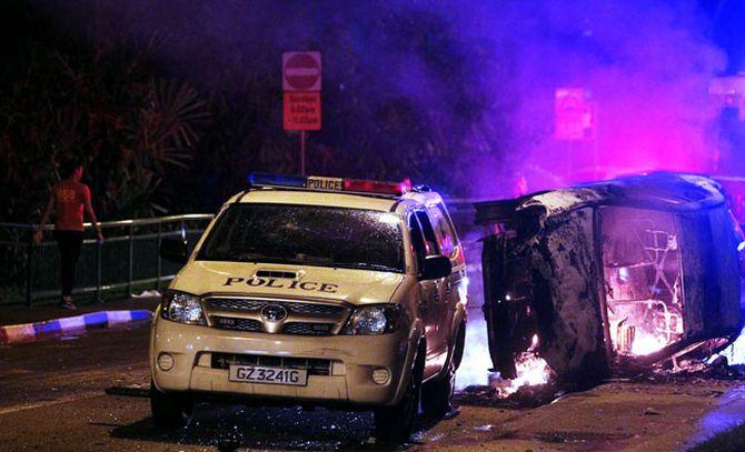 A man passes by damaged vehicles, including a police car, after a riot in Singapore's Little India district.