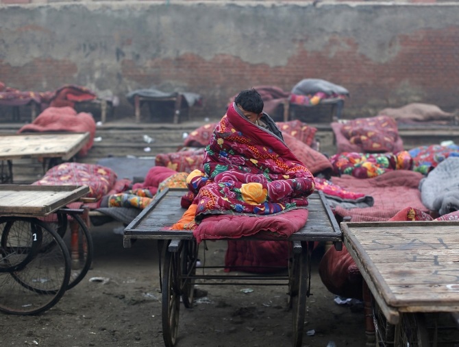A migrant labourer sits under a quilt at an open space on a cold winter morning in the old quarters of Delhi