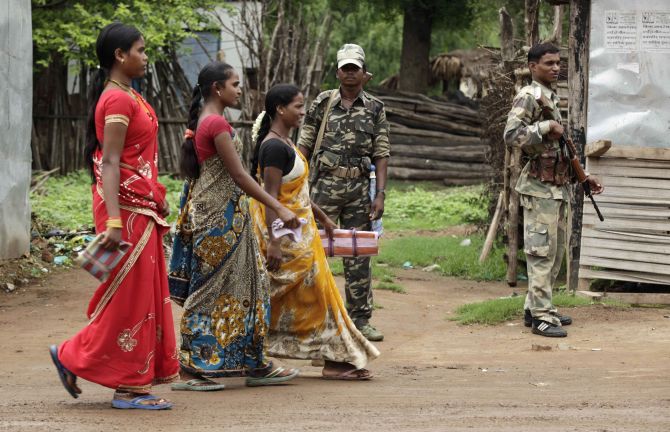 Government-backed militias stand guard as women walk past in Awapalli village in Chhattisgarh