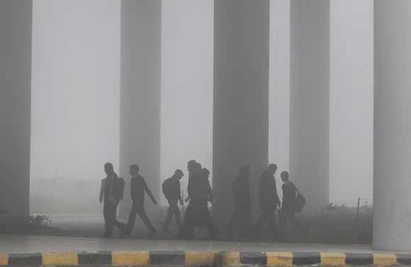 Airport staff walk towards the main terminal amid heavy fog in New Delhi