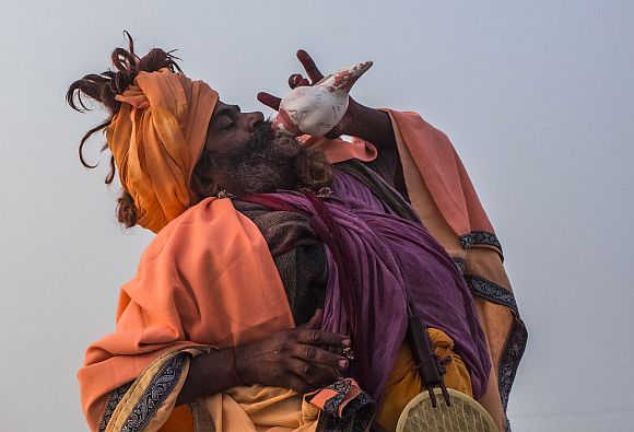 A sadhu blows a conch shell on the banks of the Ganga river during the Maha Kumbh Mela