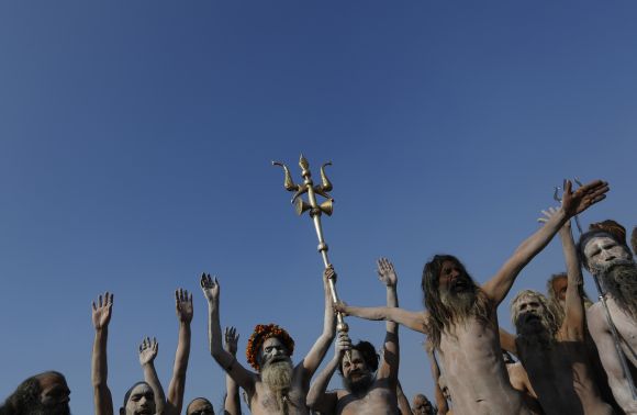 Sadhus gesture as one of them holds a trishul after taking a dip during the second