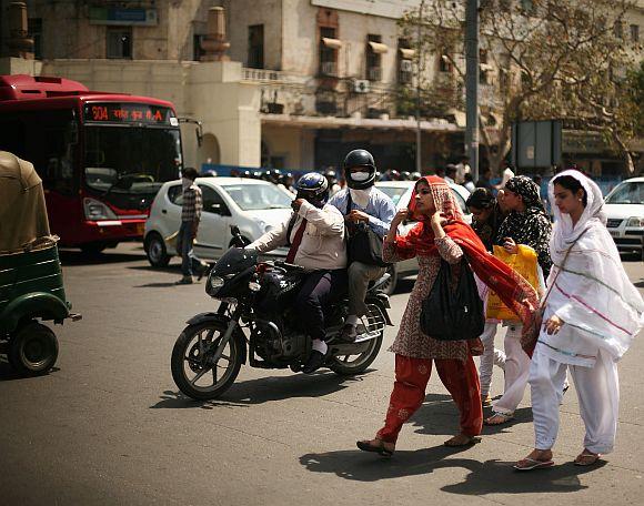 A motorcycle passes a group of ladies as they cross a street in New Delhi