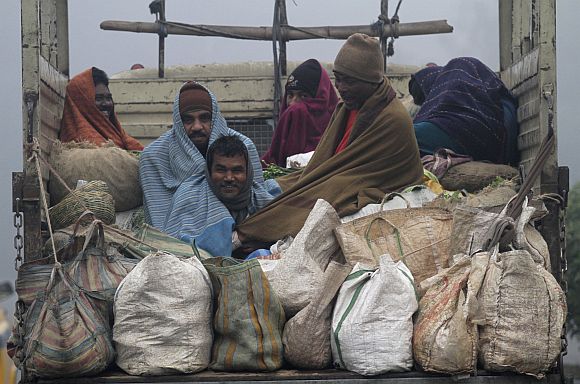 Vendors covered in blankets sit in the back of a supply truck after buying vegetables from a market on a cold winter morning