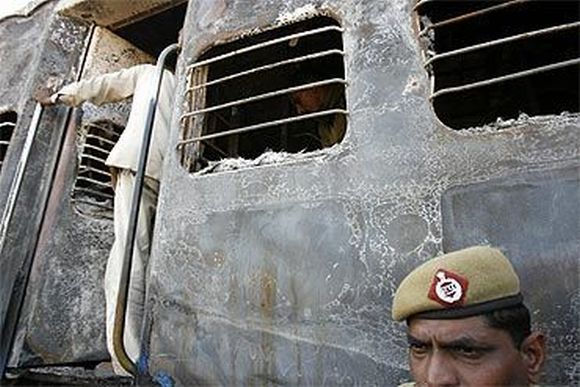 A policeman stands outside a burnt carriage of Samjhauta Express train near Panipat on February 2007 following two bomb blasts