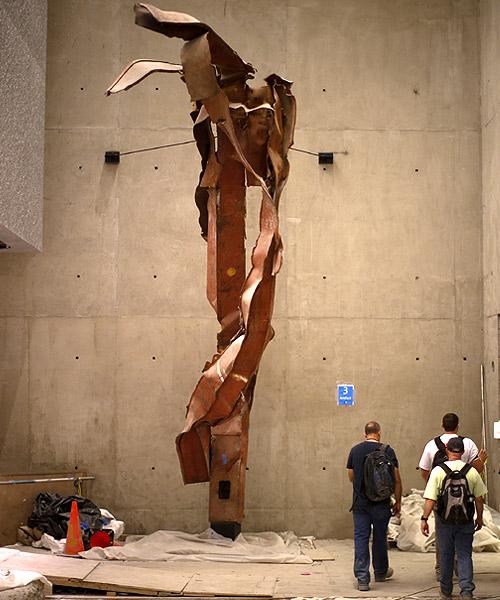 Construction workers walk past steel facade segments, also known as 'Impact Steel', that were torn apart when hijacked United Flight 175 tore into the South Tower of the World Trade Center on September 11, 2001, as it hangs inside a center passage area of the 911 MemorialMuseum, which is under construction, at the WorldTradeCenter site in New York