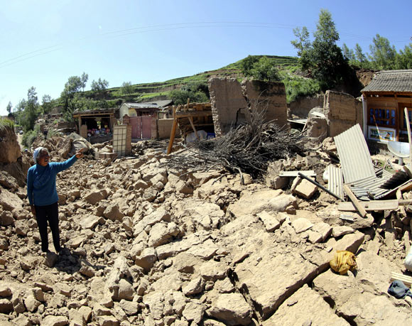 A woman points at her collapsed home