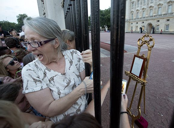 Crowds of people try to look at a notice formally announcing the birth of a son to Britain's Prince William and Catherine, Duchess of Cambridge, placed in the forecourt of Buckingham Palace, in central London