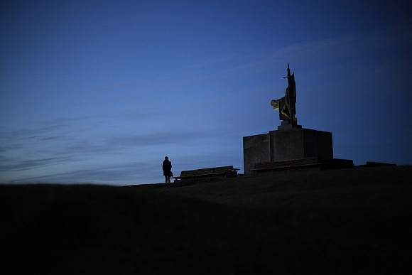A man stands next to the monument of Ingolfur Arnason, known as Iceland