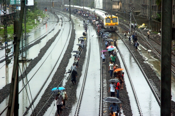 Commuters walk on the tracks as trains come to an halt because of the downpour near Sion station