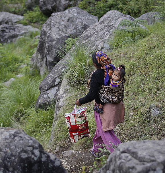 A woman carrying a baby on her back walks down a hill during a rescue operation at Govindghat