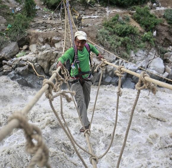 A man crosses a rope bridge over the Alaknanda river during rescue operations in Govindghat, Uttarakhand