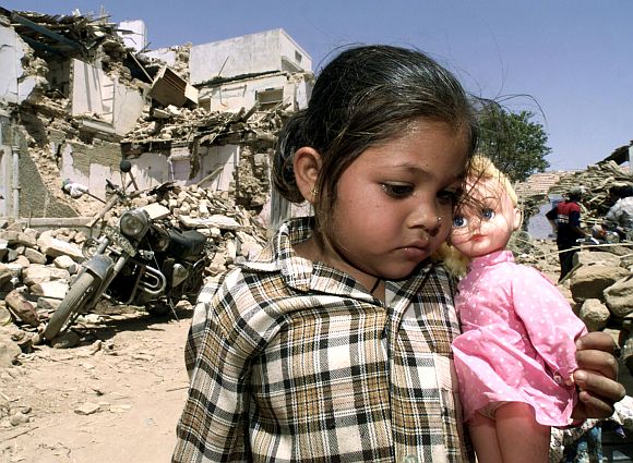 Putya, five-years-old, holds her doll while standing in front of the ruins of her house in Bhuj, April 3, 2001