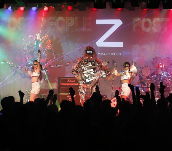 Members of the robot rock band Z-Machines, guitarist Mach (C), keyboardist Cosmo (L) and drummer Ashura perform with dancers