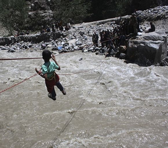 Indian Army personnel rescue a stranded child with the help of ropes through the flooded waters of a river