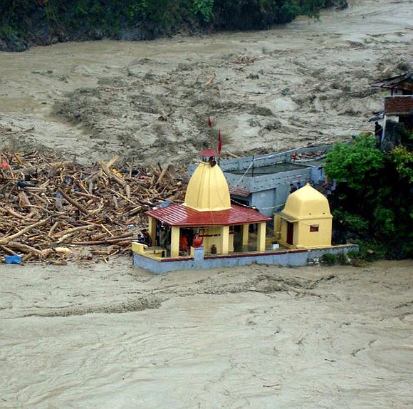 Debris carried by floodwaters of the River Alaknanda crashes against a temple in Chamoli district