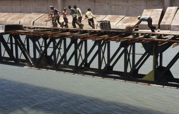 Labourers drag an iron girder across a bridge under construction over the Vembanad Lake in Kochi