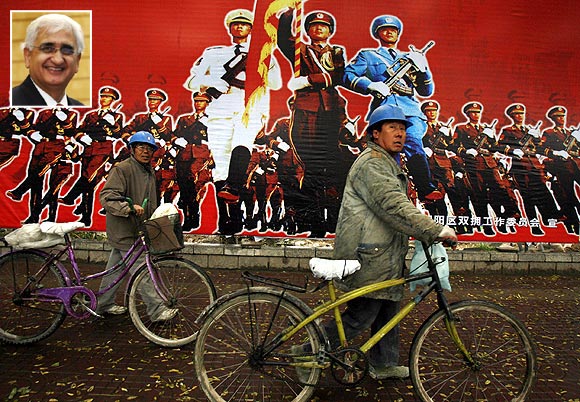 Workers push their bicycles past a billboard promoting China's People's Liberation Army in Beijing and (inset) Salman Khurshid
