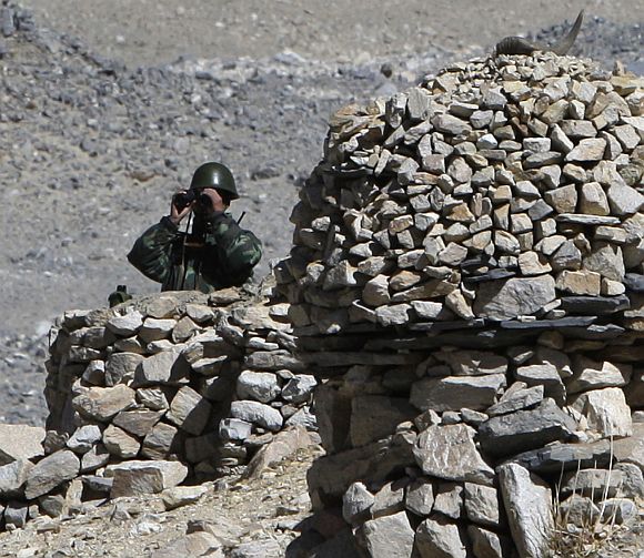 A Chinese border policeman looks through binoculars while manning an observation post made of rocks next to Rongbo Monastery in the Tibet Autonomous Region