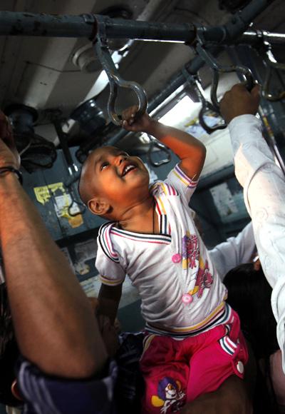 A child tries to hold onto the handrails in a crowded suburban train during rush hour in Mumbai