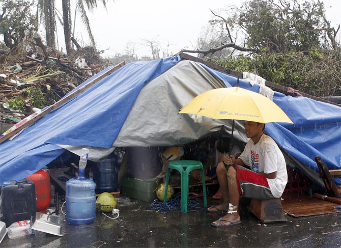 A typhoon victim sits under an umbrella outside a makeshift tent