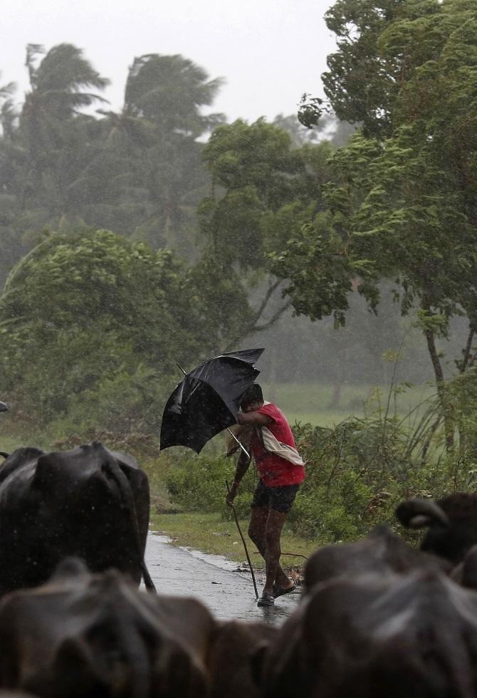 A boy tries to cover himself with an umbrella during heavy rain brought by Cyclone Phailin in Ichapuram town in Srikakulam district