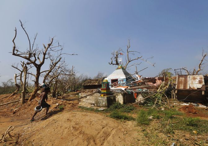 A man carries his belongings on Monday as he walks past a damaged temple after Cyclone Phailin hit Arjyapalli village
