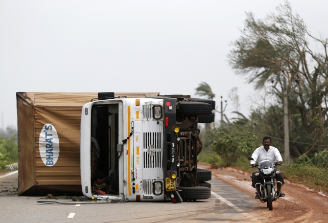 A man rides his motorbike past an overturned vehicle after Cyclone Phailin hit Gopalpur in Ganjam district in Odisha